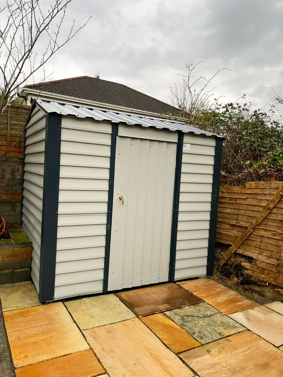 A white shed is sitting on a tiled patio in a backyard.