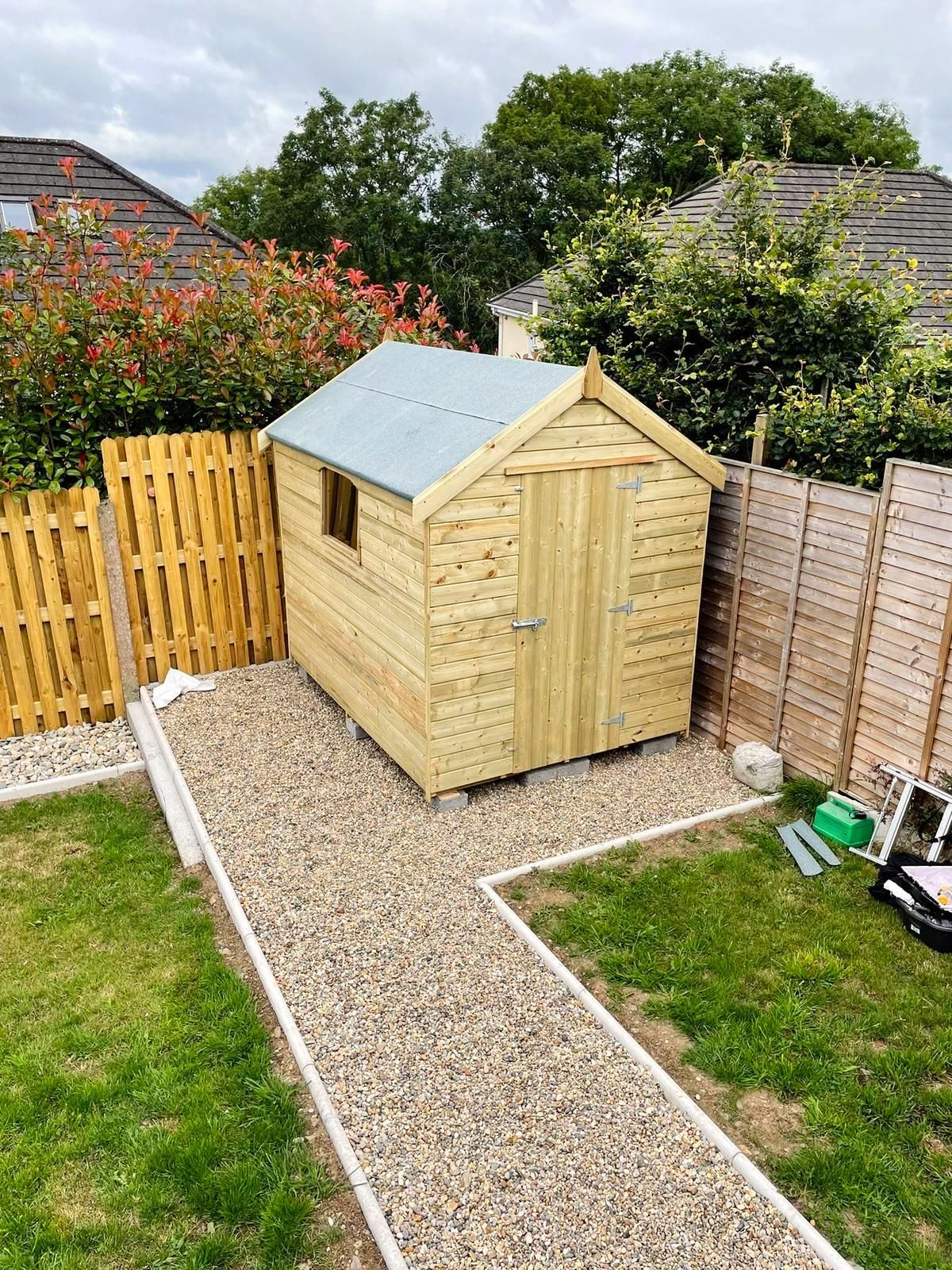 A wooden shed is sitting in the middle of a backyard next to a gravel path.