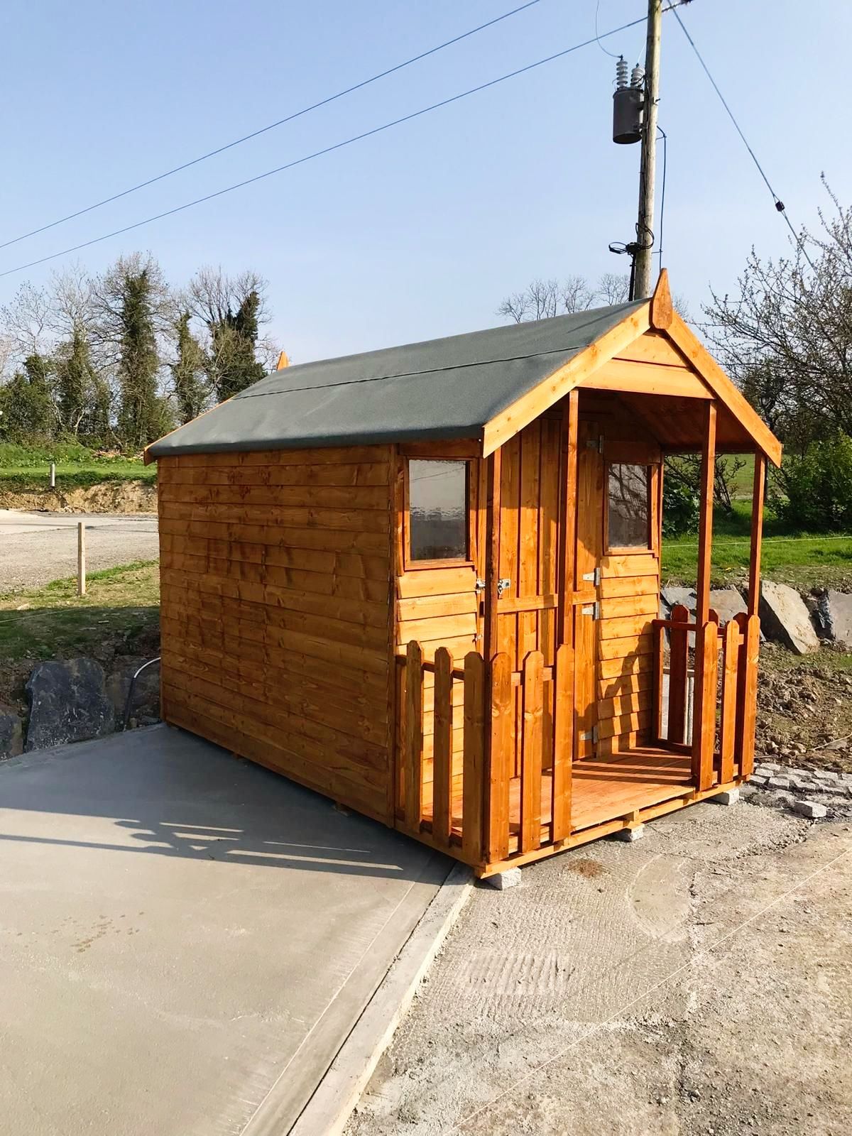 A small wooden shed with a green roof and a porch