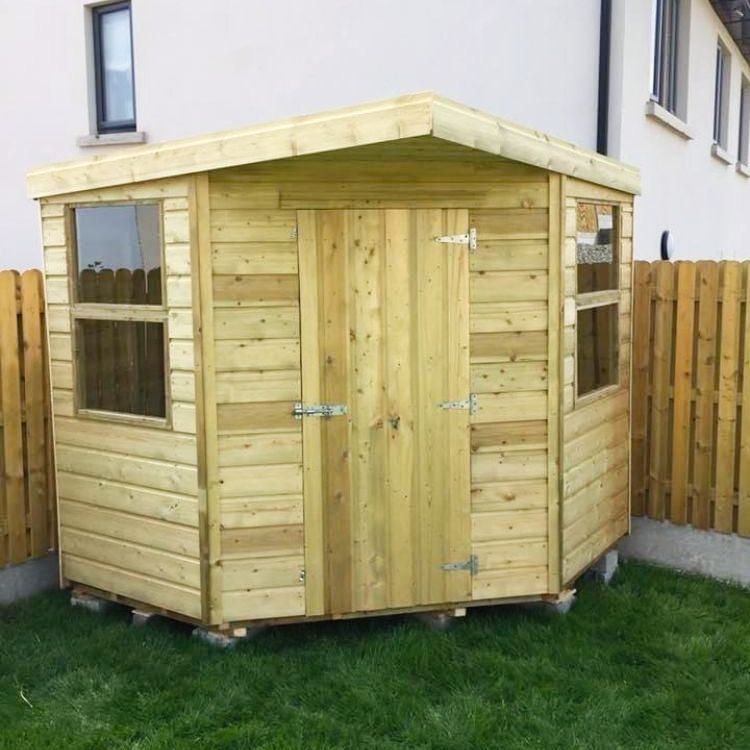 A small wooden shed is sitting in the grass in front of a house
