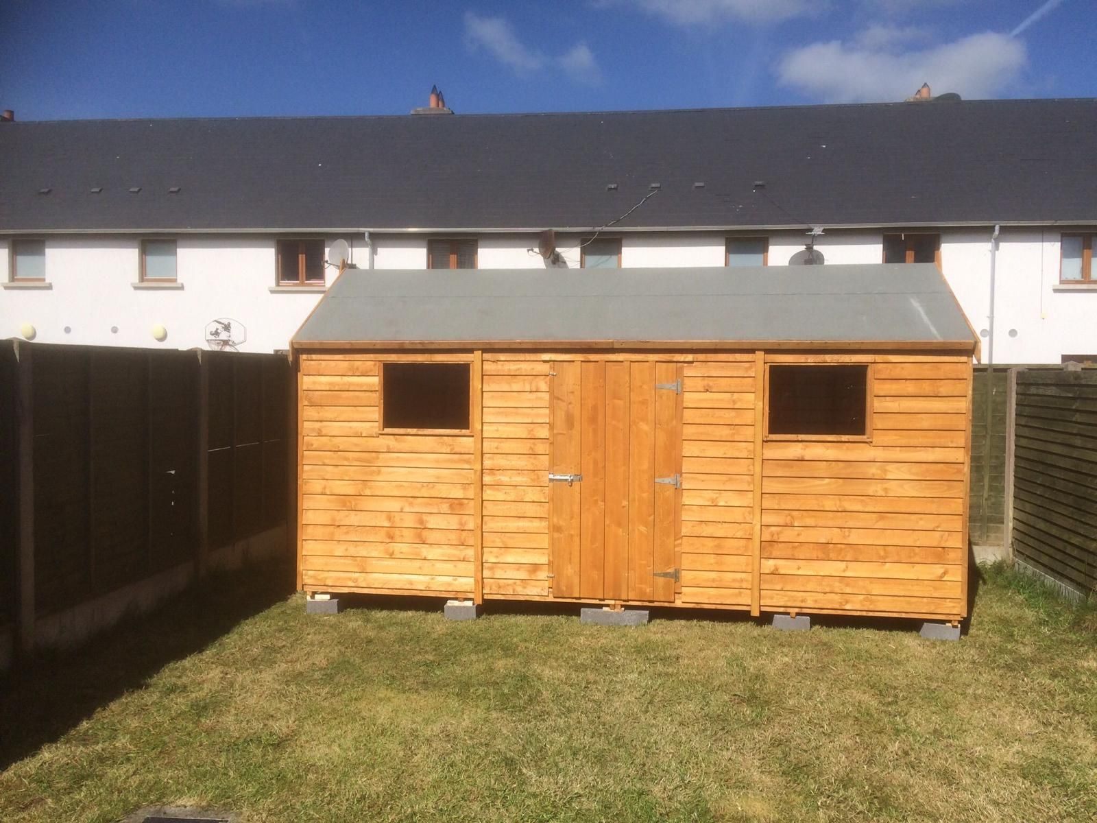 A wooden shed is sitting in the grass in front of a house.