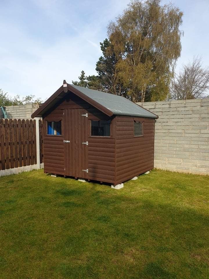 A brown shed is sitting in the middle of a lush green yard.