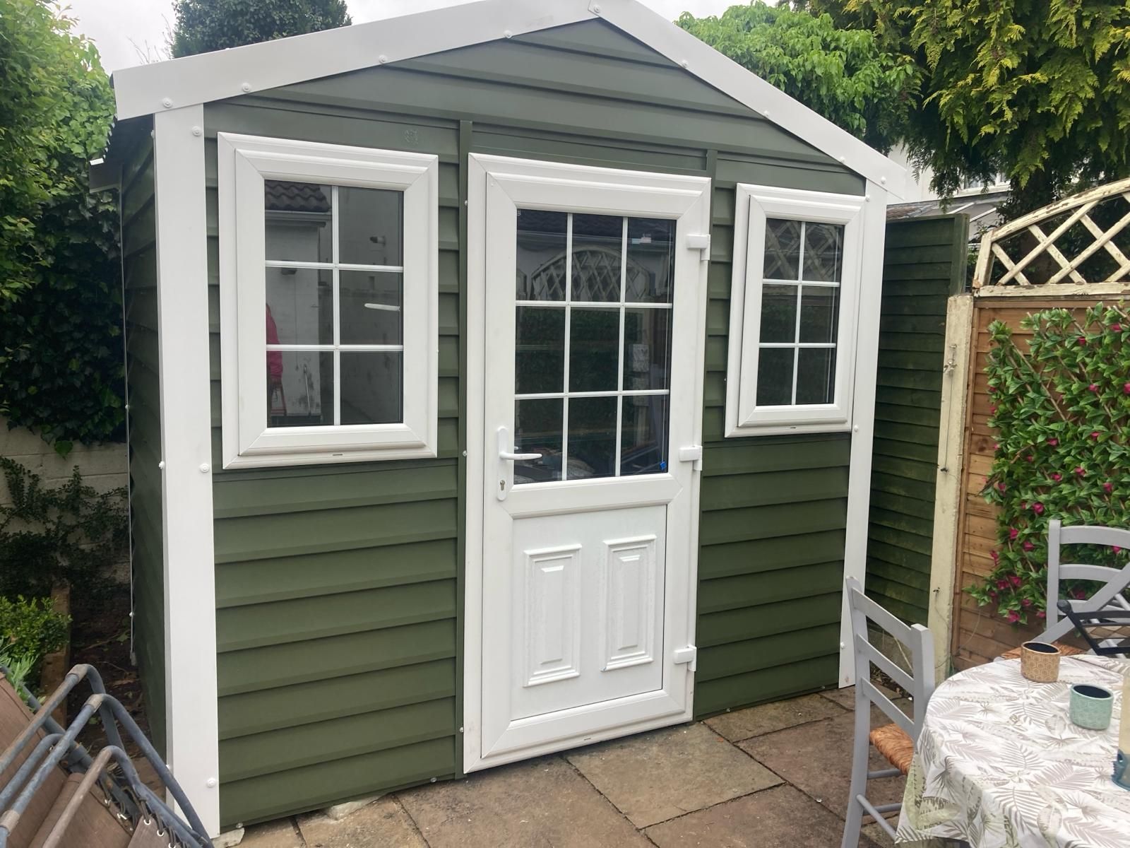 A white shed is sitting in the middle of a grassy yard next to a tree.