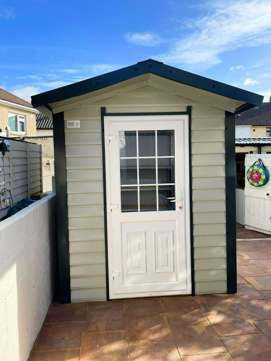 A small white shed with a black roof and a white door.