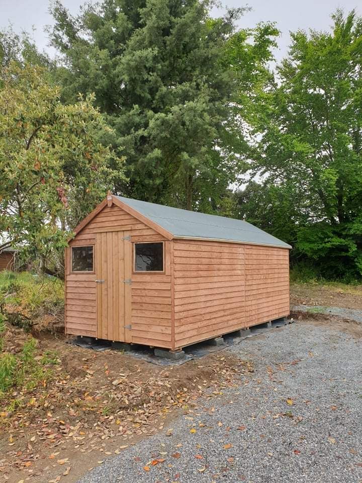 A small wooden shed is sitting in the middle of a gravel driveway.