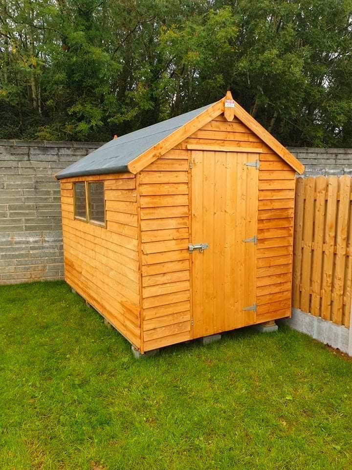A wooden shed is sitting on top of a lush green lawn next to a wooden fence.
