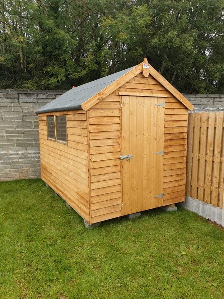 A wooden shed is sitting in the grass next to a wooden fence.