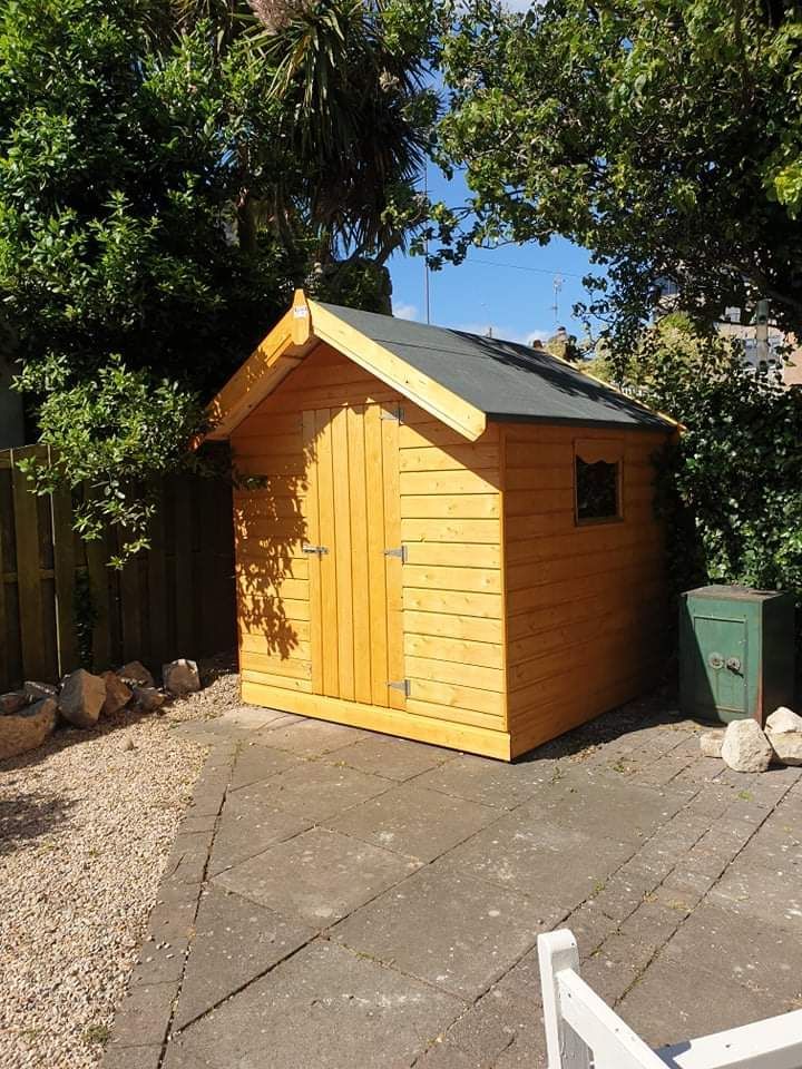 A small wooden shed is sitting in the middle of a gravel driveway.