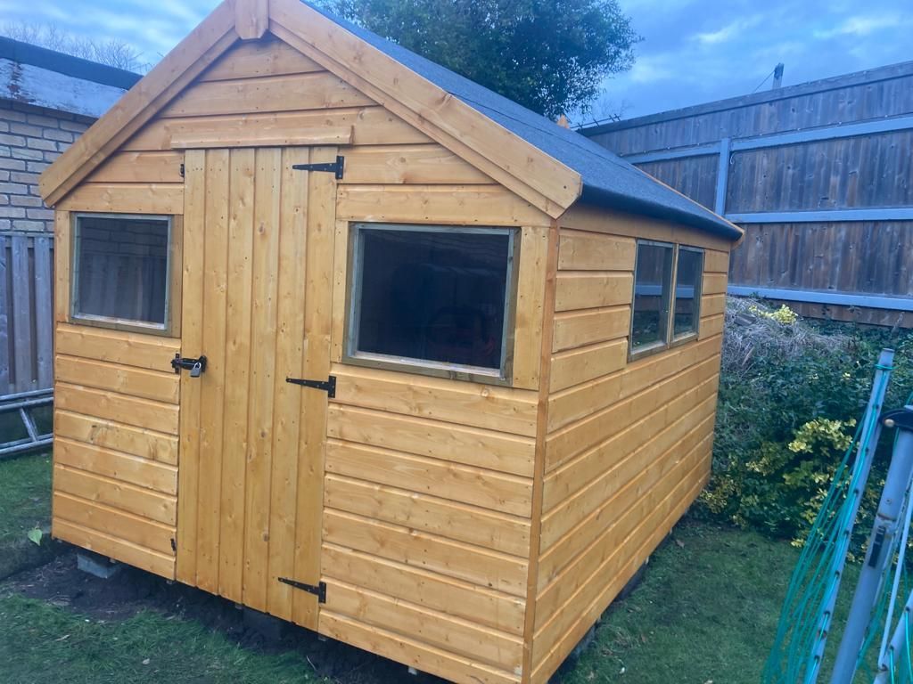 A wooden shed with two windows is sitting in the grass.