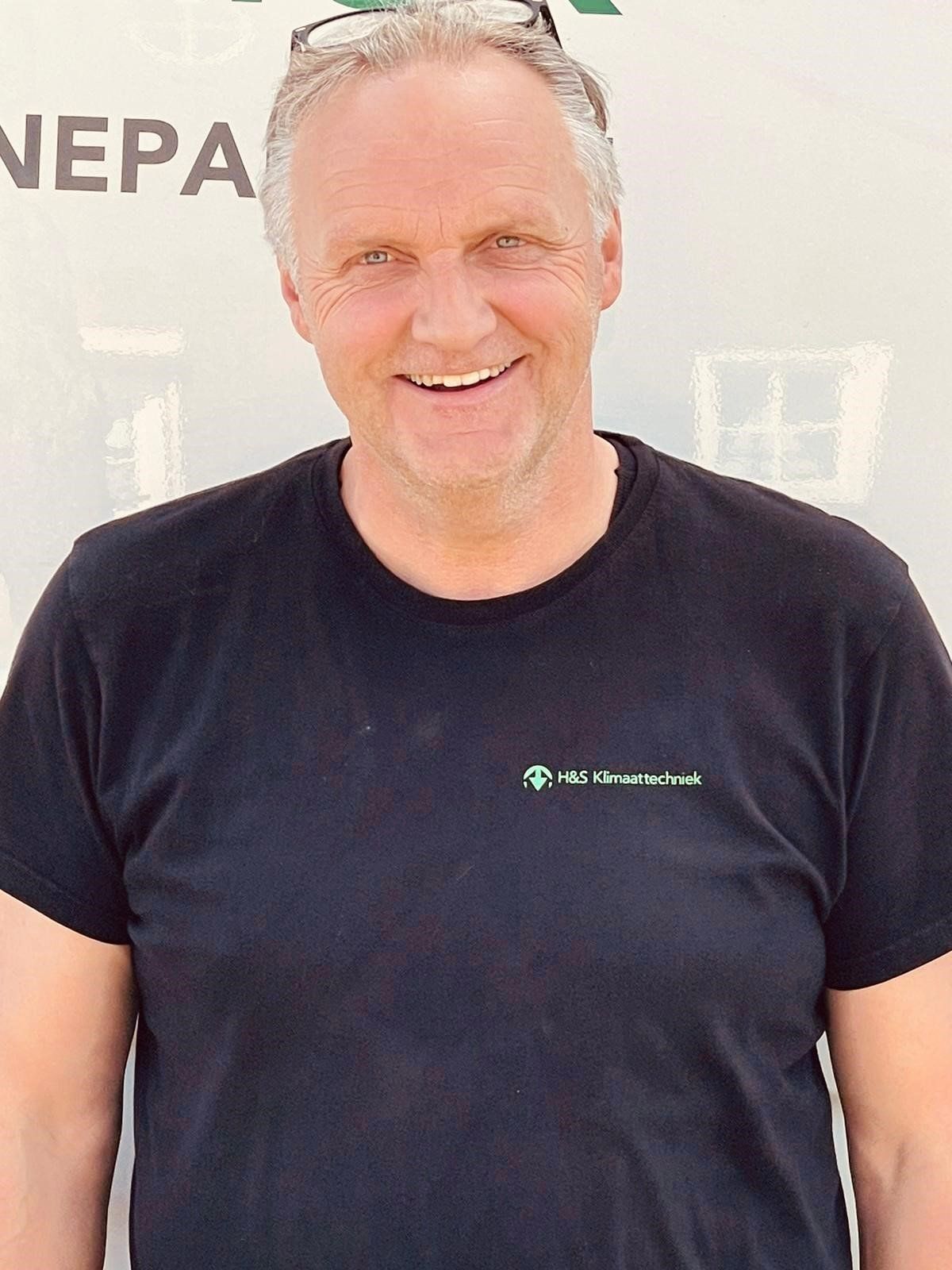 Een man in een zwart T-shirt lacht naar de camera.