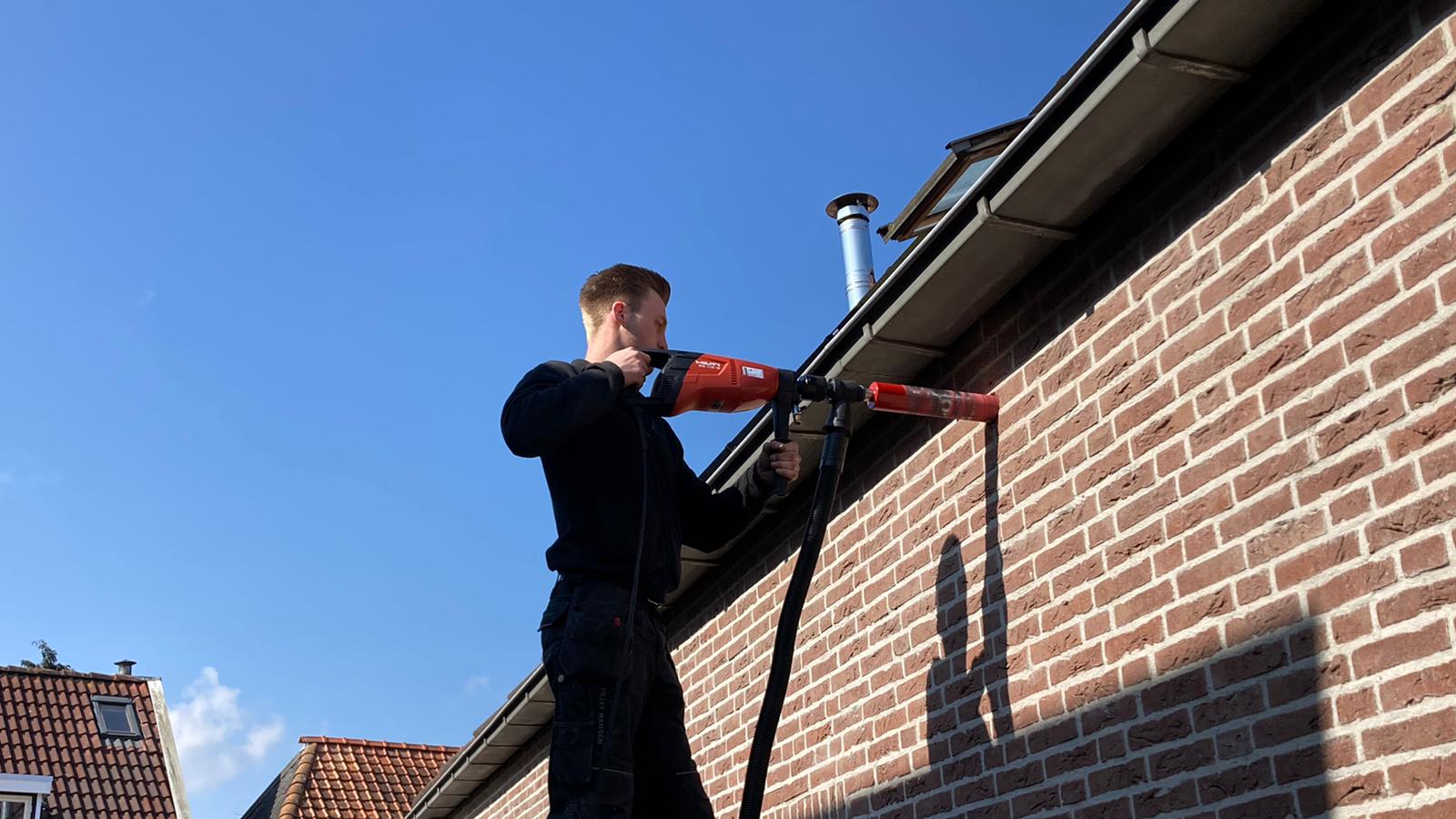 Een man is met een boormachine aan het werk aan een bakstenen muur.