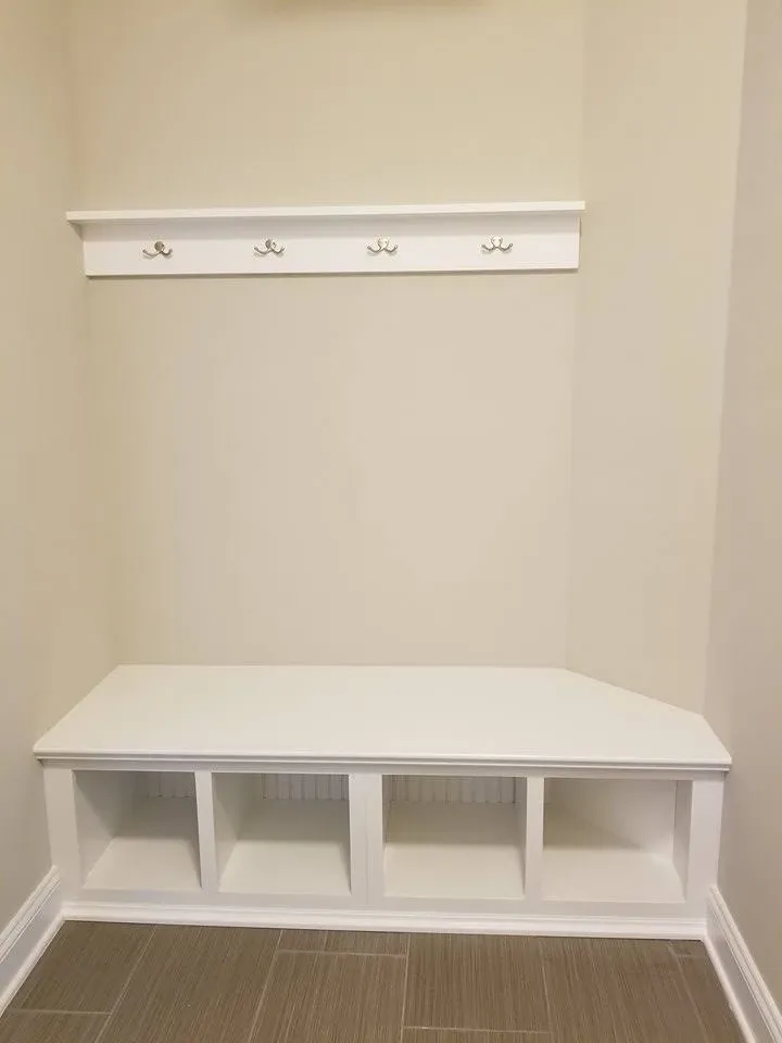 A white bench with hooks on the wall in a hallway.
