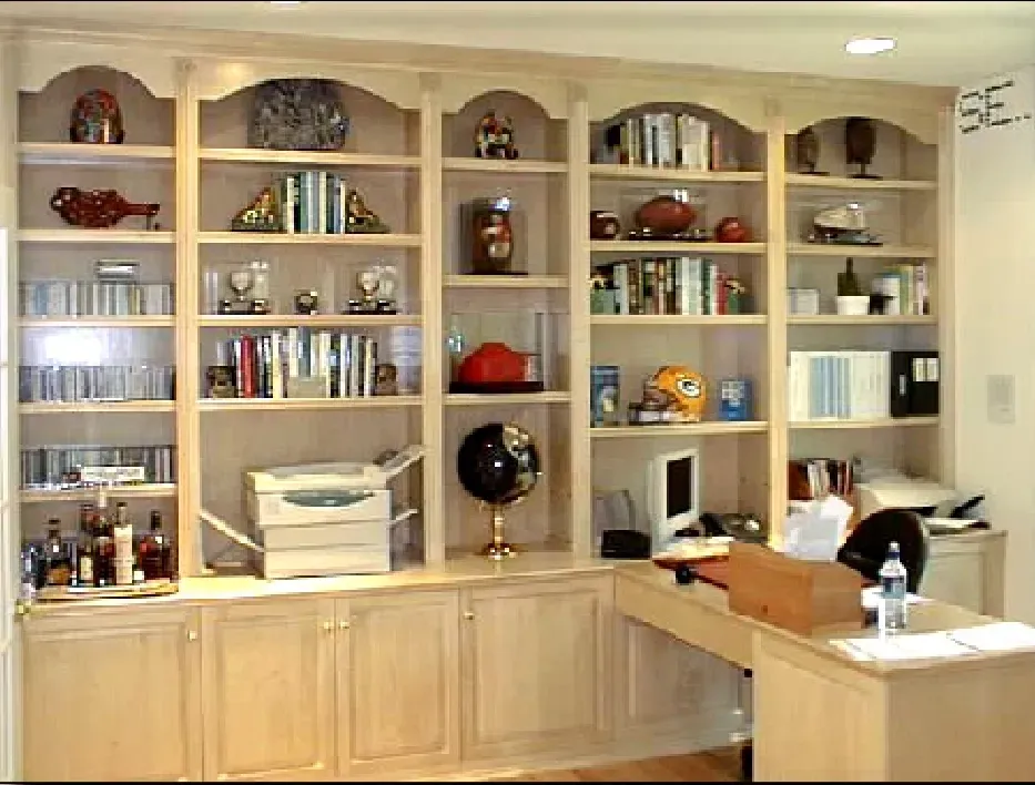 A man sits at a desk in front of a wall of shelves with se written on it