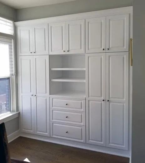 A room with a lot of white cabinets and drawers and a window.