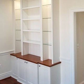 A white bookshelf with glass shelves and wooden cabinets in a room.