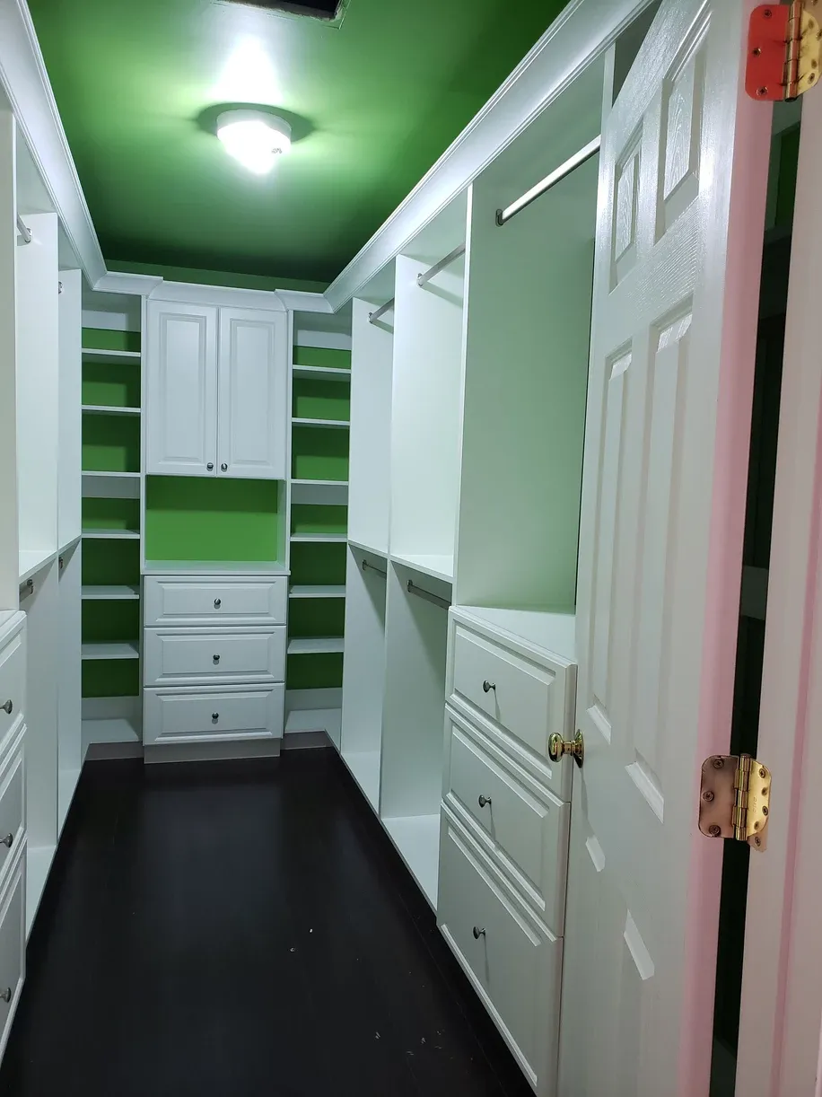 A walk in closet with green ceiling and white cabinets