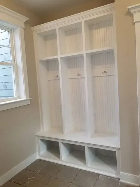 A room with a bench , shelves , hooks and a window.