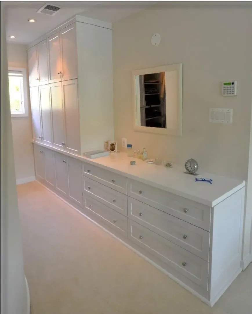 A bathroom with white cabinets and drawers and a mirror