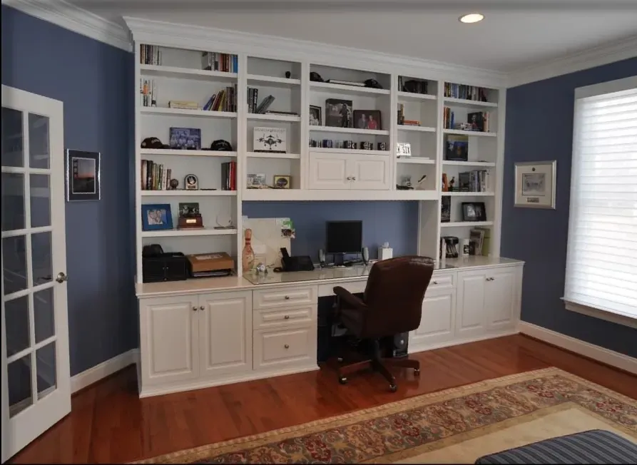 A home office with blue walls and white cabinets