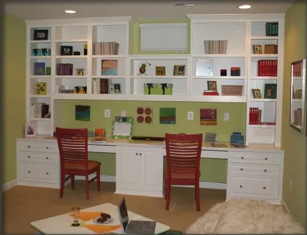 A room with two desks and shelves has a laptop on the table