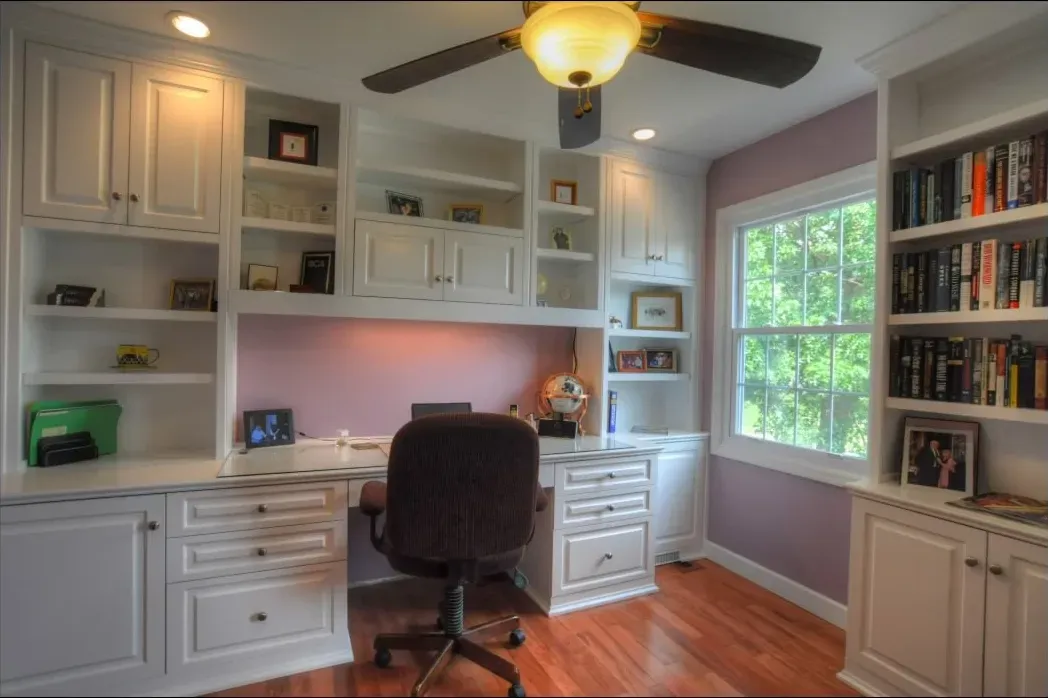 A home office with purple walls and white cabinets