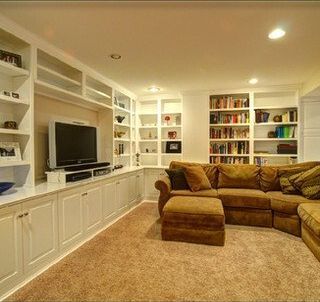 A living room with a couch , ottoman , television and shelves.