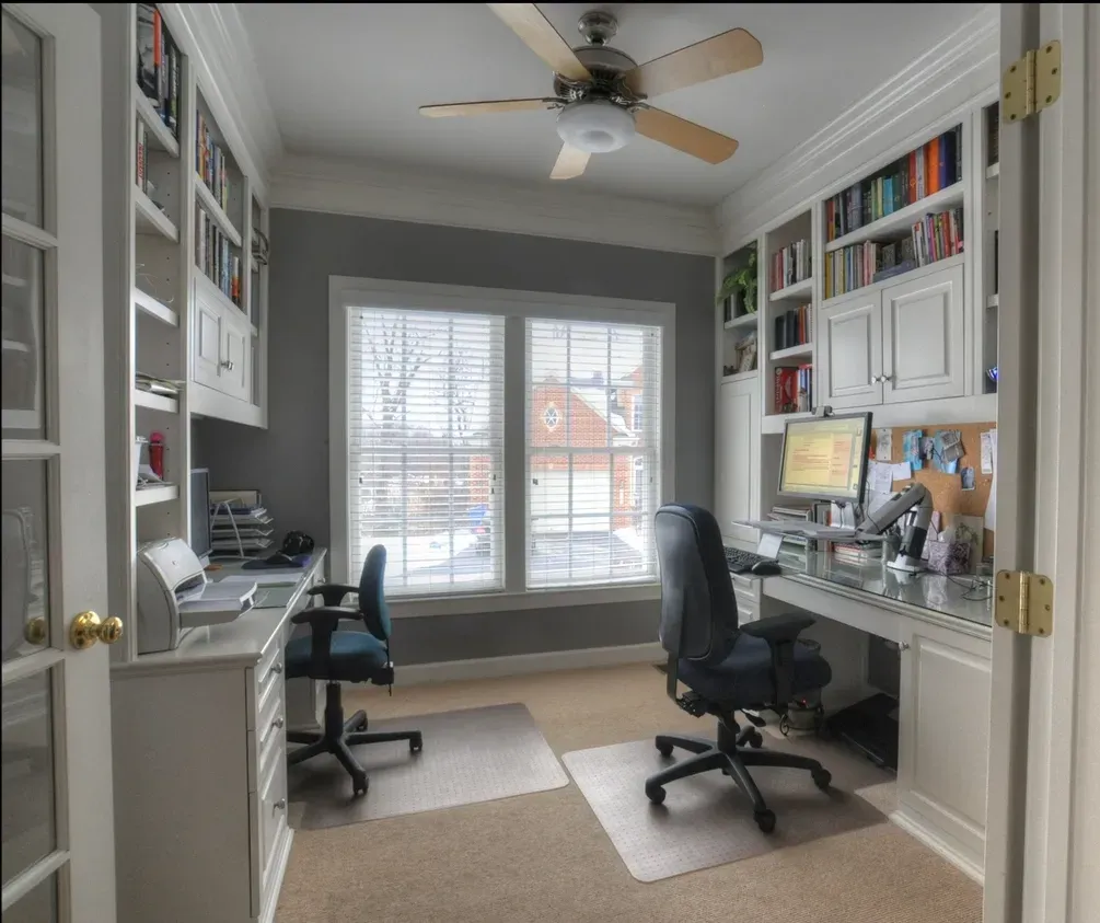 A home office with two desks and a ceiling fan