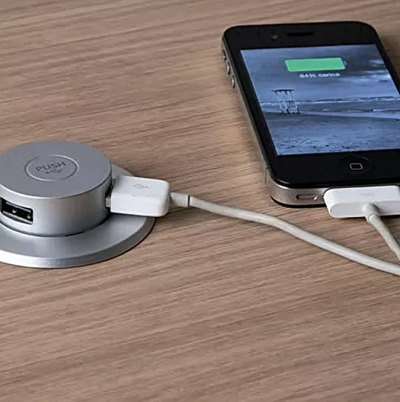 A cell phone is plugged into a usb charger on a wooden table.