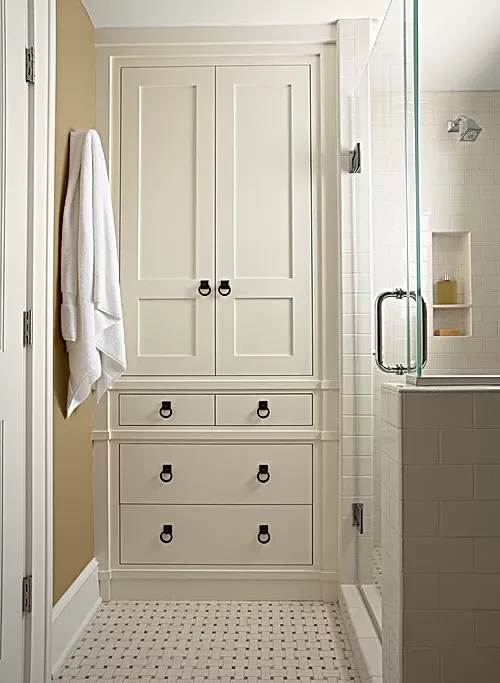 A bathroom with white cabinets and drawers and a glass shower door