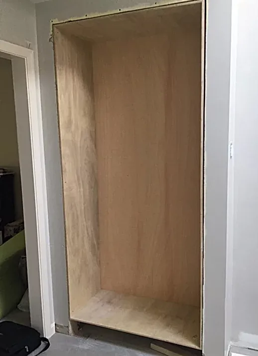 A wooden shelf is being built into a wall in a room.