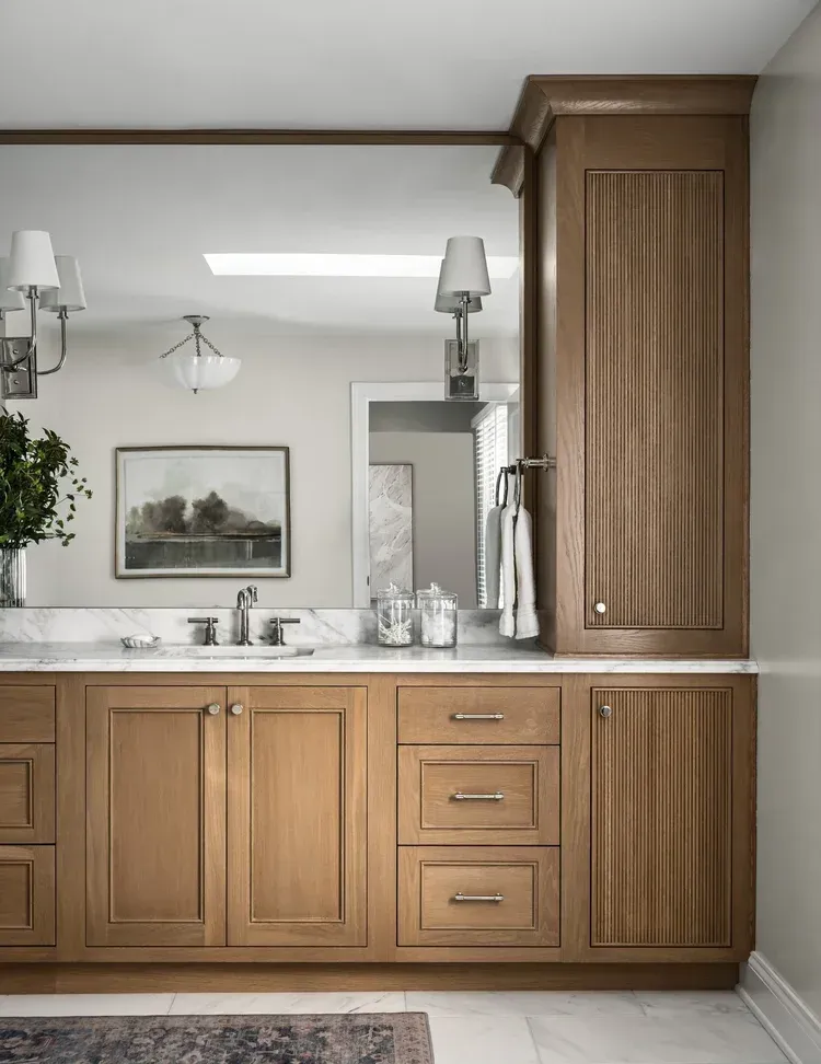 Bathroom vanity with wood cabinetry, marble countertop, and large mirror.