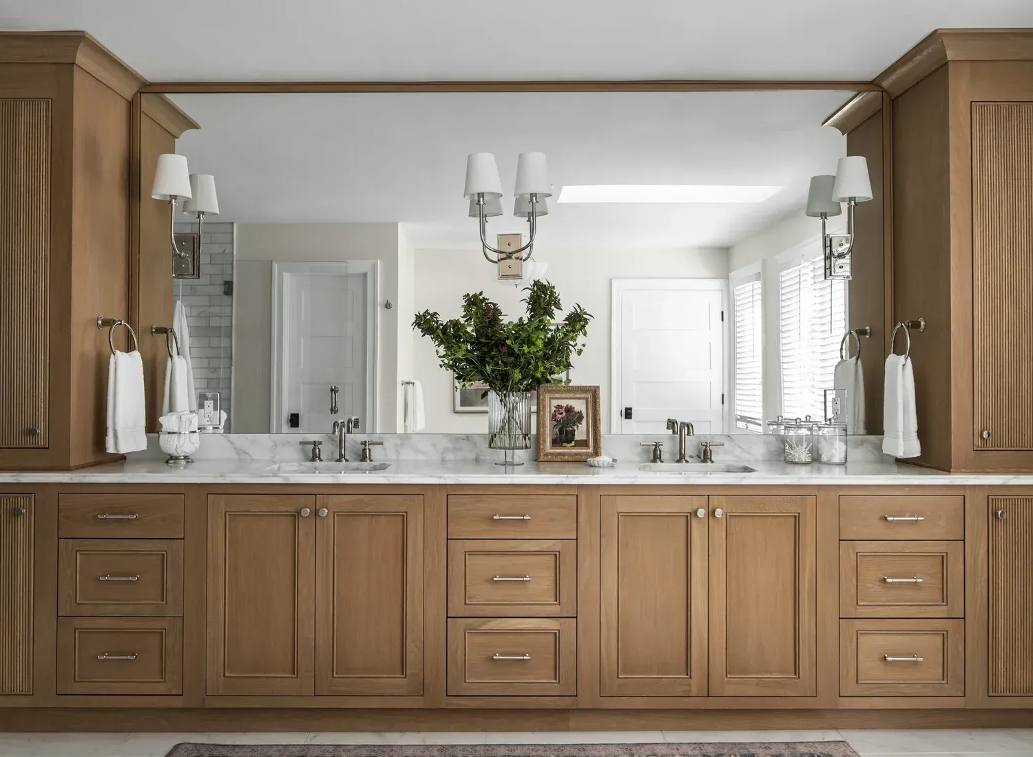 Bathroom with oak vanity, large mirror, and sconce lighting.