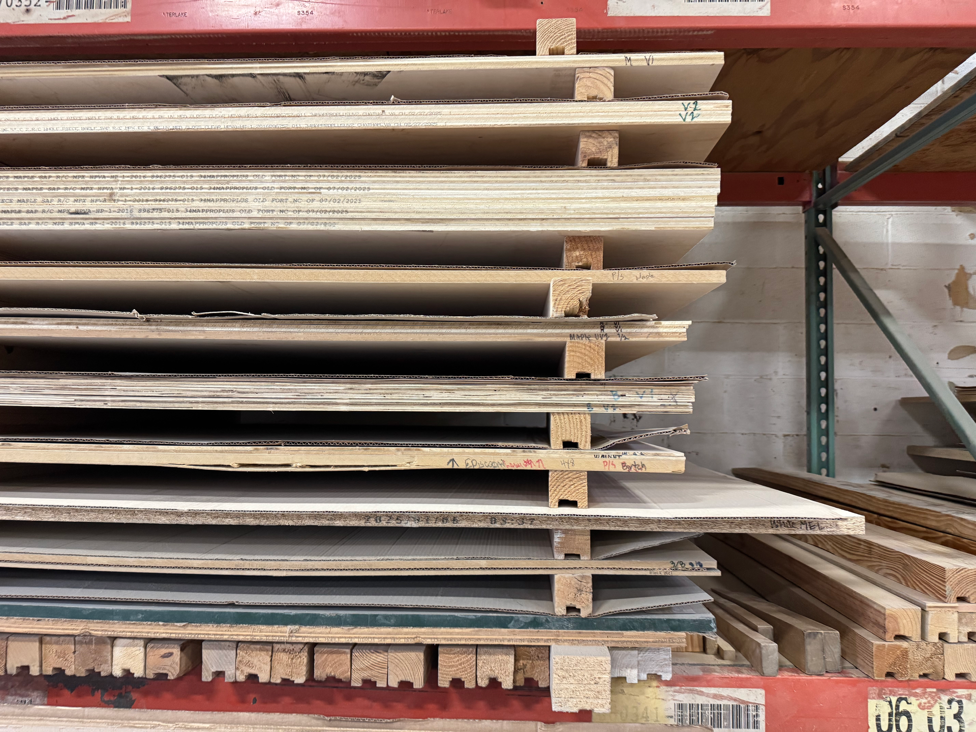 Stack of plywood sheets on a warehouse shelf, separated by wooden supports.