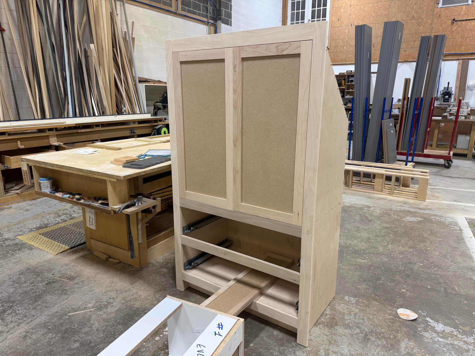 A partially constructed wooden cabinet in a workshop. The cabinet has doors and drawers.
