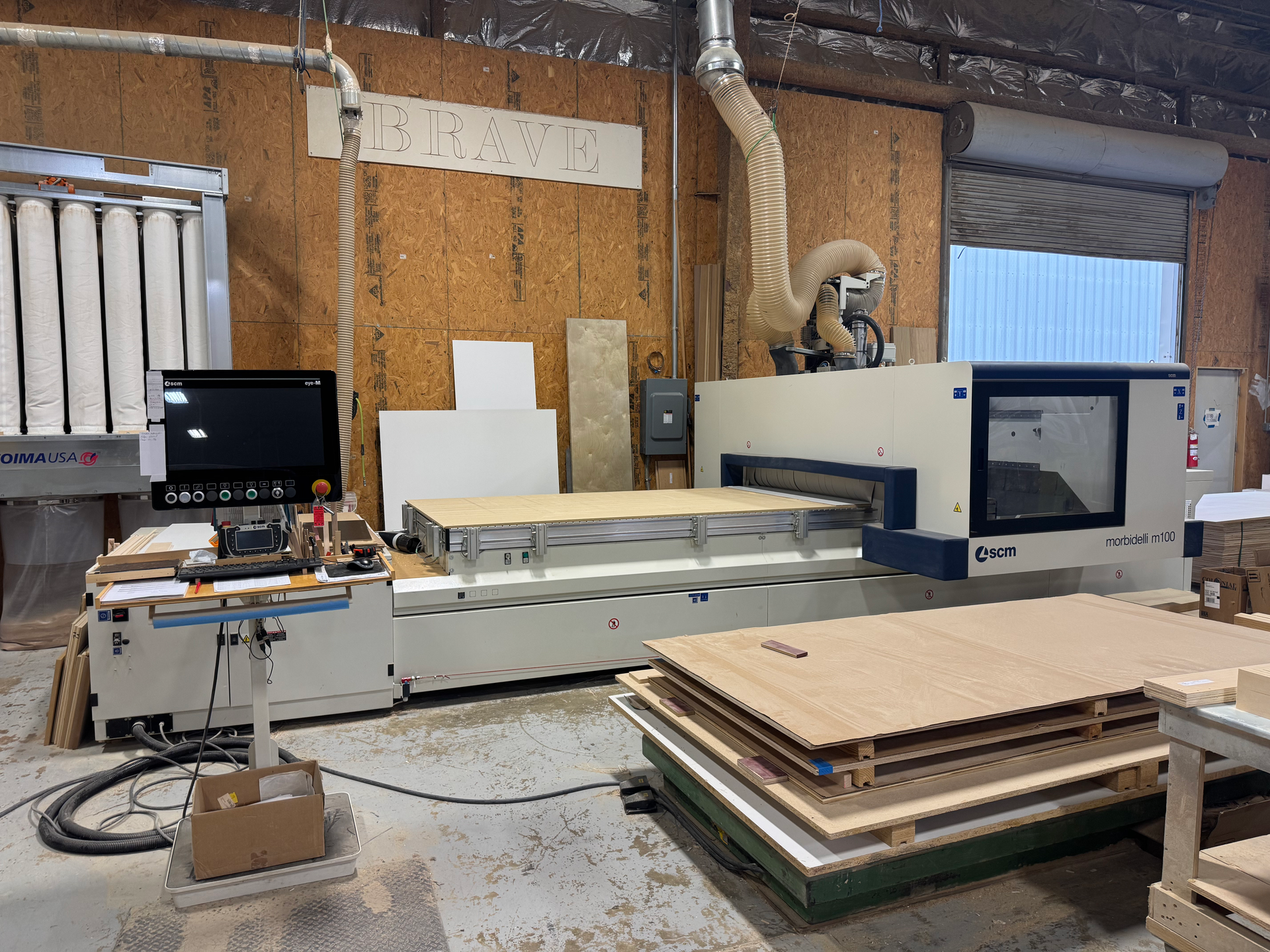 CNC machine in a workshop, cutting wood. Several wood sheets are nearby.