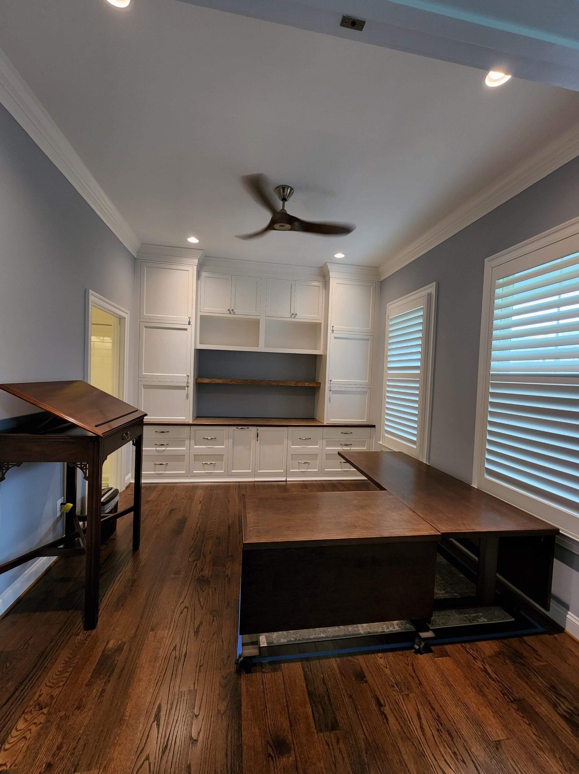 A room with a ceiling fan and shutters on the windows