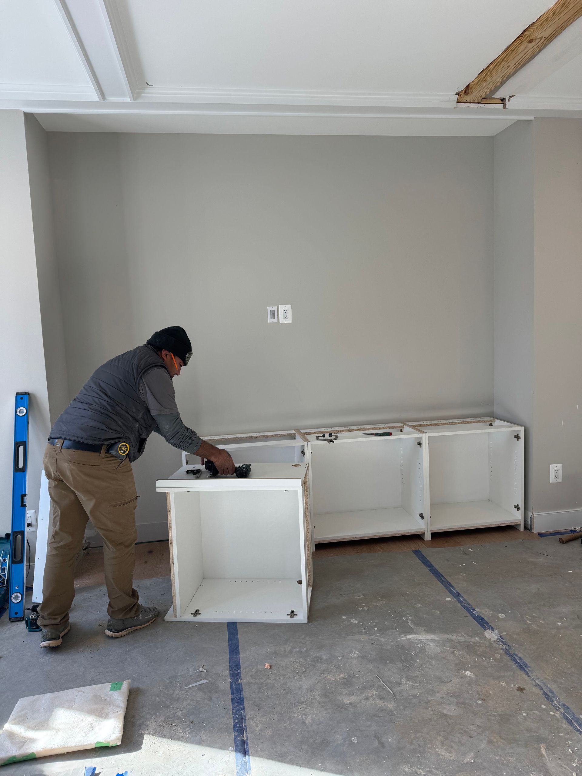 A worker installs white cabinets along a gray wall.
