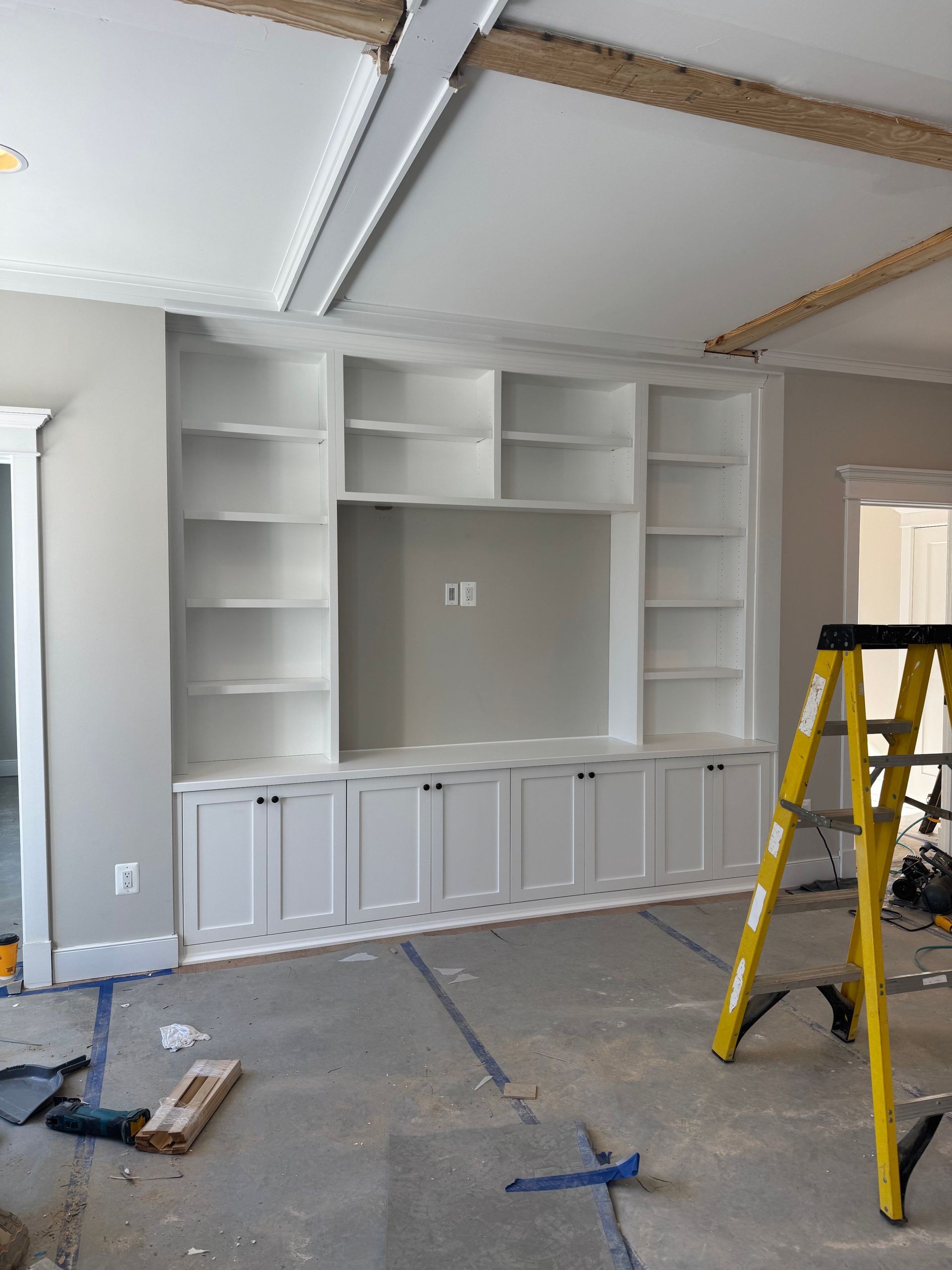 Built-in white shelving unit with doors, shelves, and TV space on a gray wall. Yellow ladder present.