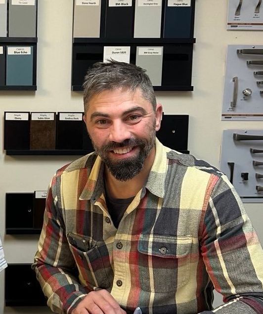 A man with a beard is smiling in front of a stone wall.