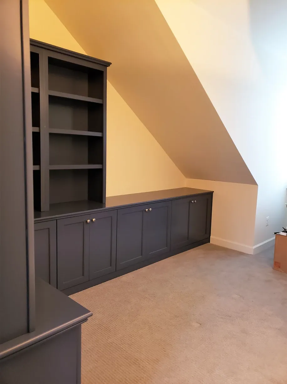A room with a slanted ceiling and black cabinets