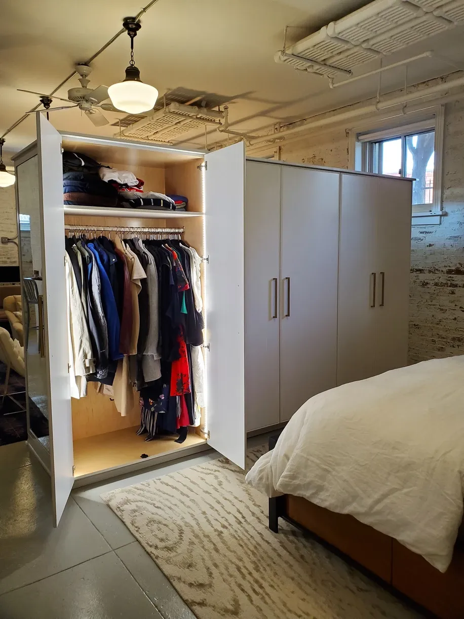 A bedroom with a closet full of clothes and a bed