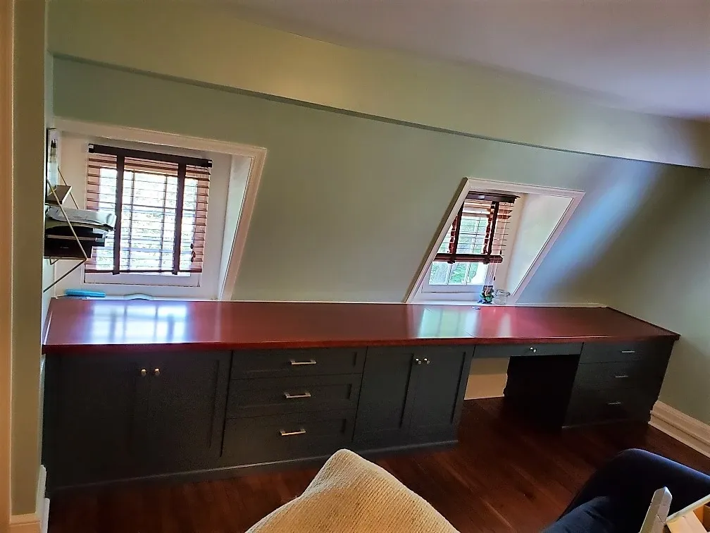 A living room with a desk and two windows