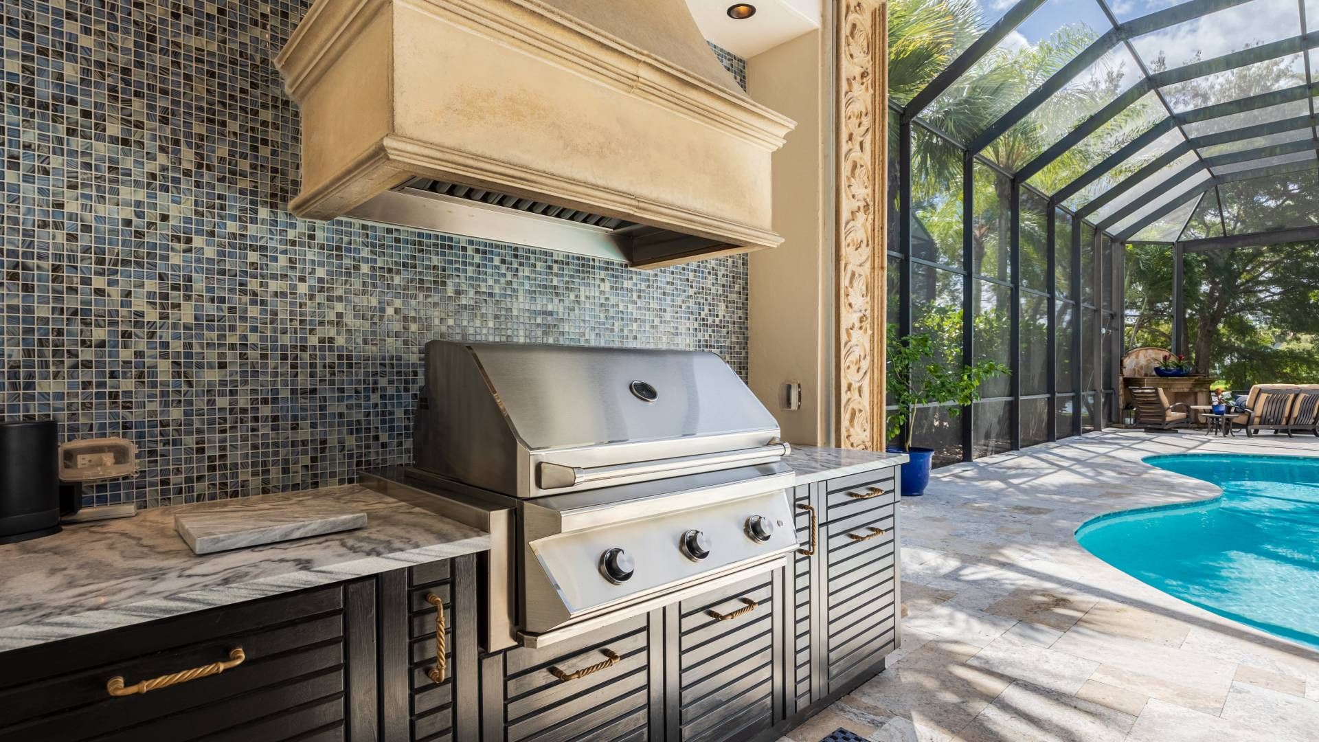 A luxury lanai design featuring an outdoor grill, fume hood, countertop, cabinets, and swimming pool