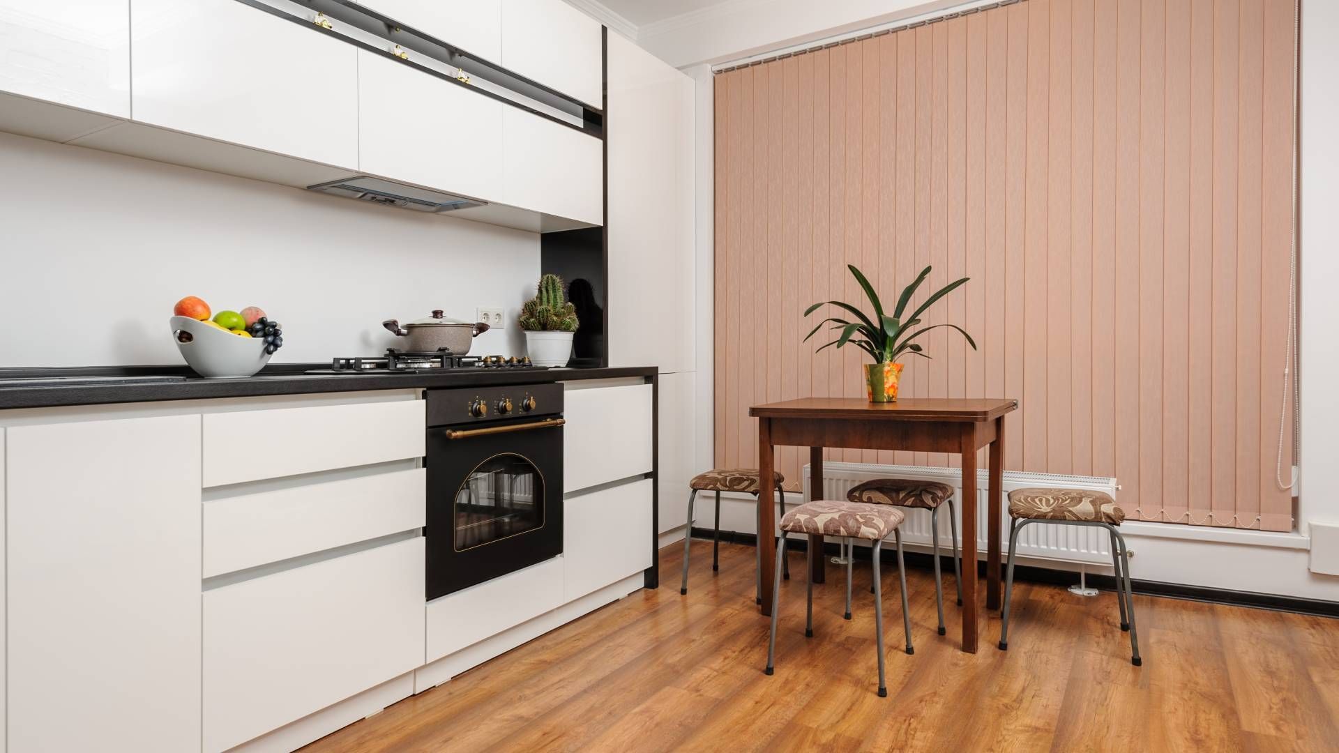 Peachy colored vertical blinds hanging from a tall and wide kitchen window with a dining table at Di