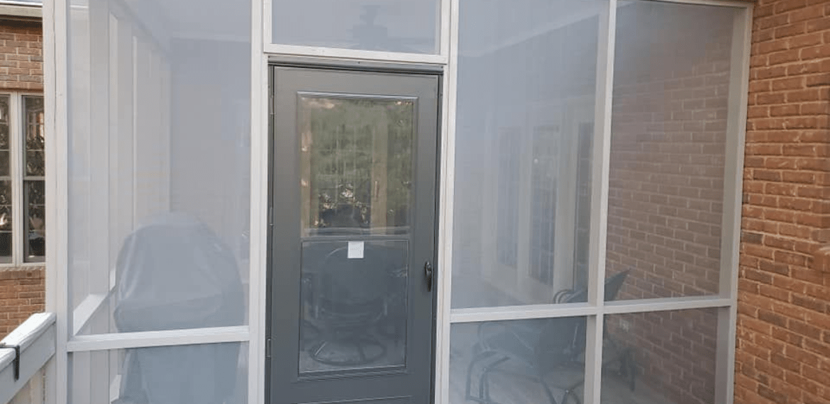 A screened porch with a gray door and brick wall