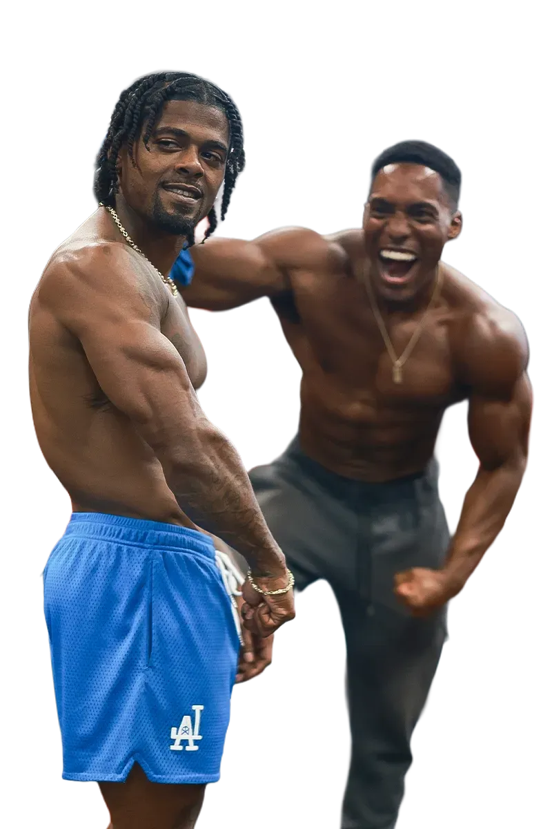 Two shirtless men standing next to each other with one wearing la shorts
