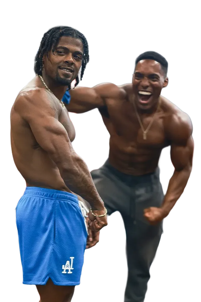 Two shirtless men standing next to each other with one wearing la shorts
