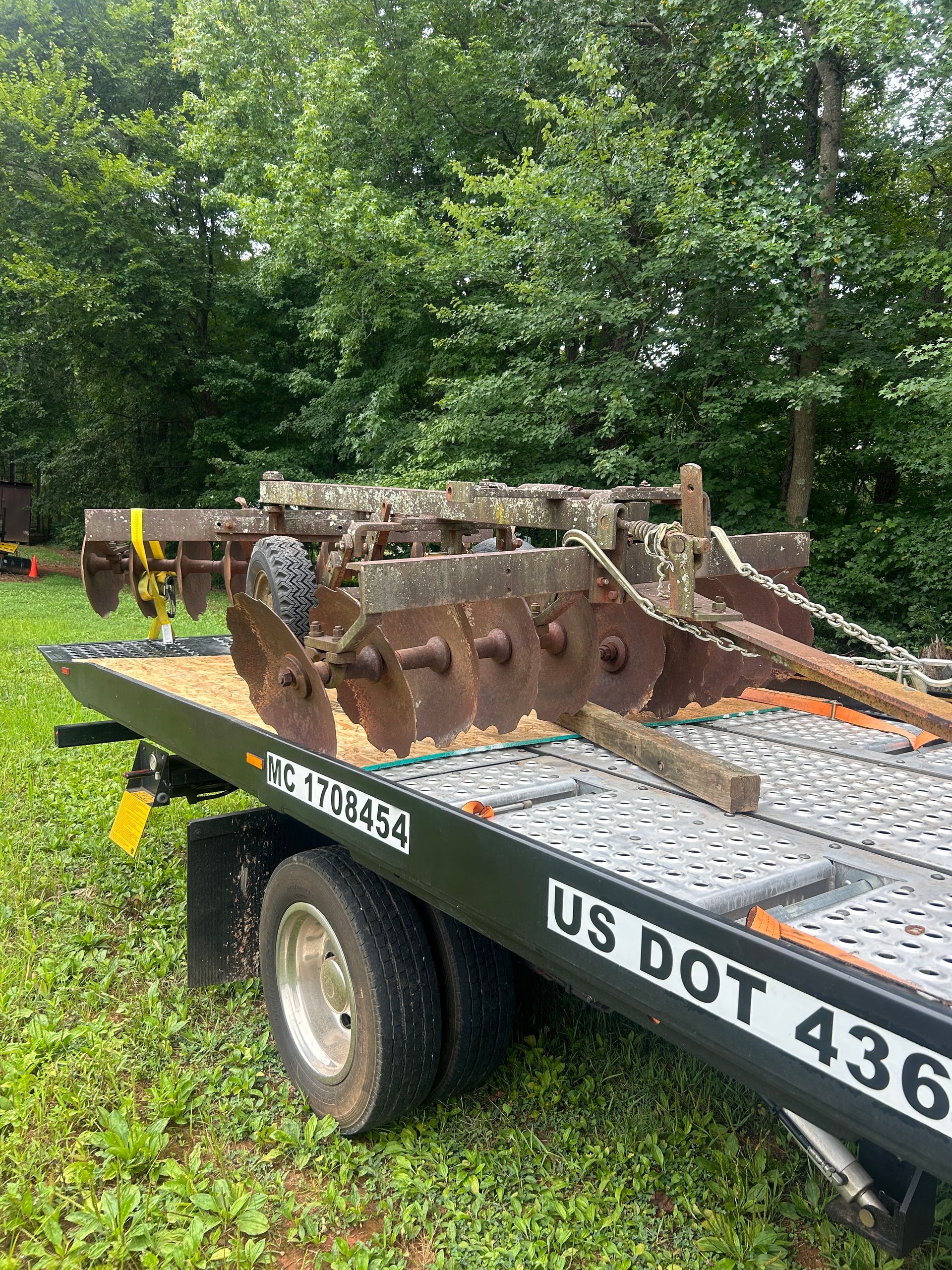 Rusty industrial machine part on a flatbed trailer parked outdoors near trees