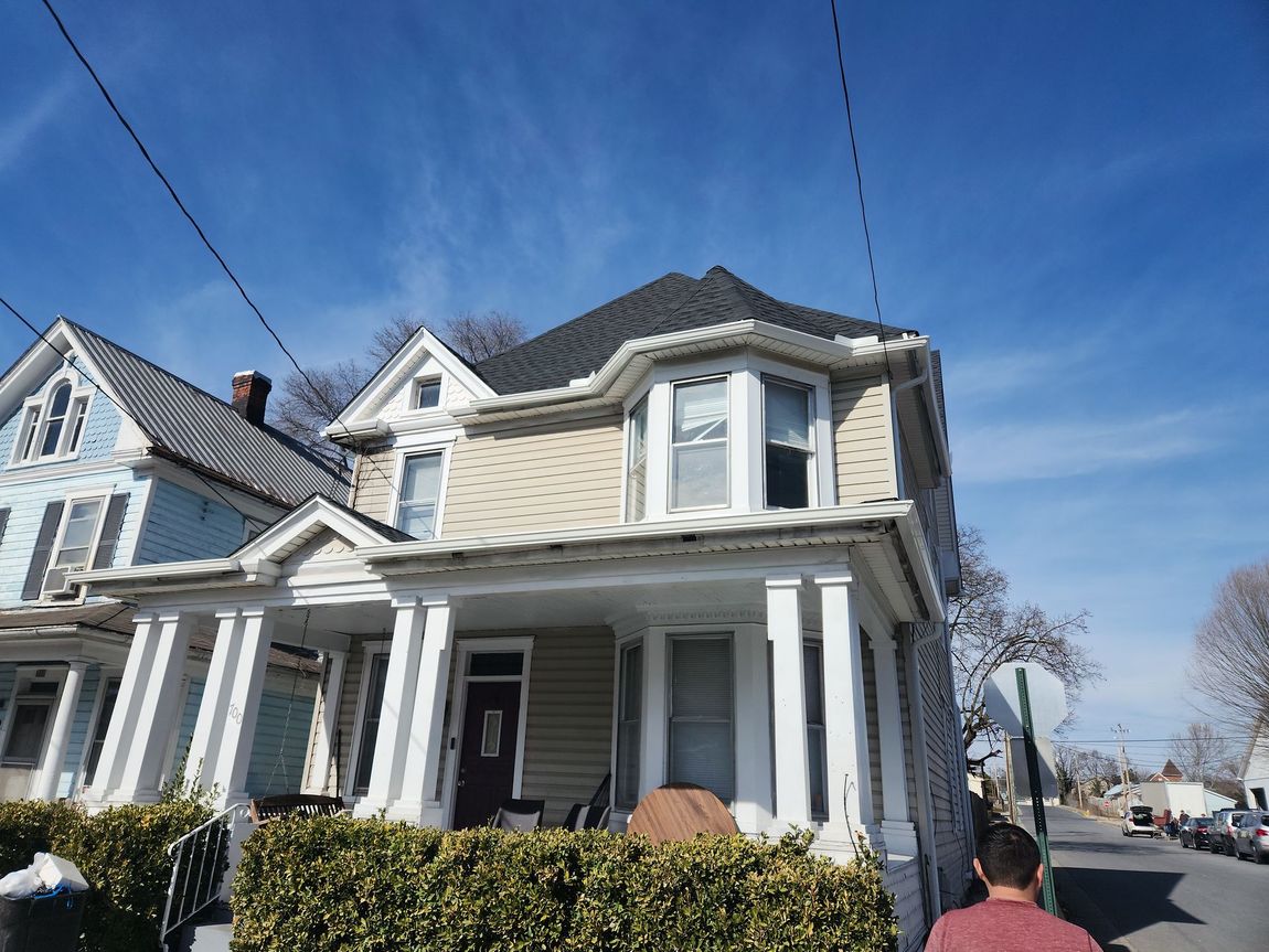 A man in a red shirt is standing in front of a house.