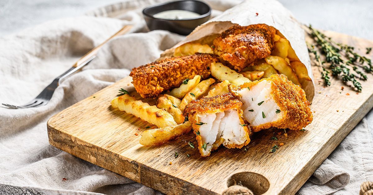 a wooden cutting board topped with fried fish and french fries .